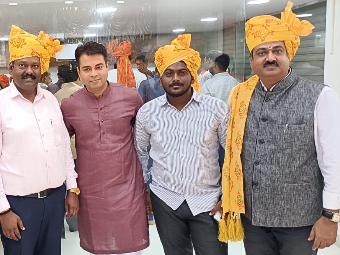 Sunil Keshary, wearing a yellow pagri, stands on the right among a group of people indoors; all are dressed in traditional attire, and several others also wear matching yellow turbans.