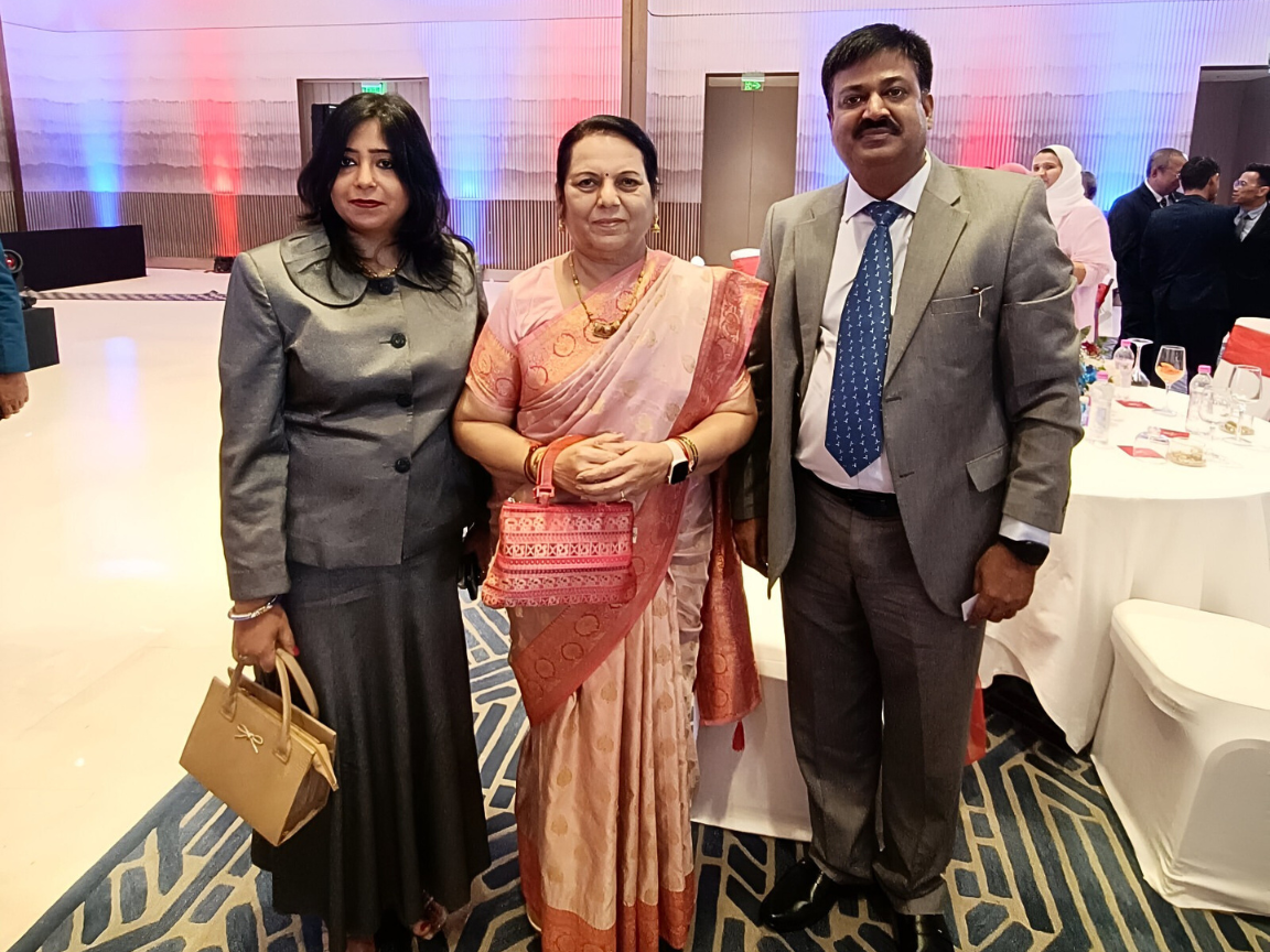 Sunil Keshary and his wife Alpana Keshary are standing on either side of Nilam Gorhe, posing for a photo together at Trident Hotel during a Russia Day celebration, with formal attire and decorated tables in the background.