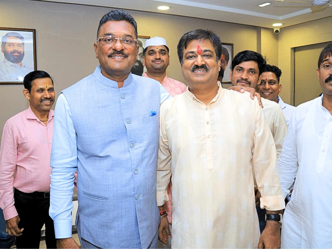 Shiv Sena leader Partap Sarnaik (left, light blue waistcoat) and Sunil Keshary (right, light yellow kurta) are posing with a group of male supporters or party workers in an indoor office setting. Sarnaik and Keshary are smiling prominently in the foreground, with portraits of other leaders visible on the wall behind them, indicating a political meeting or gathering.