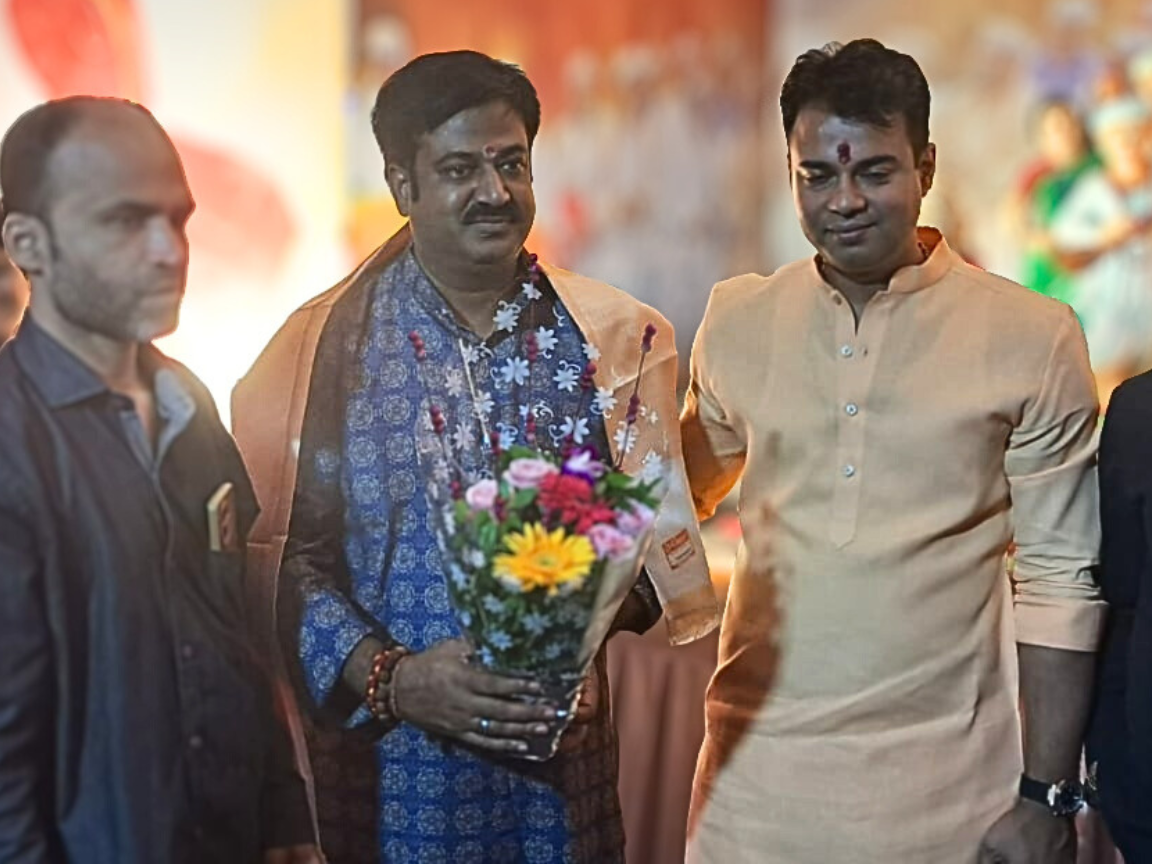 Sunil Keshary and Sankar Jha are at an event; Sunil Keshary is holding a bouquet of colorful flowers while people stand beside him in a warmly lit space.