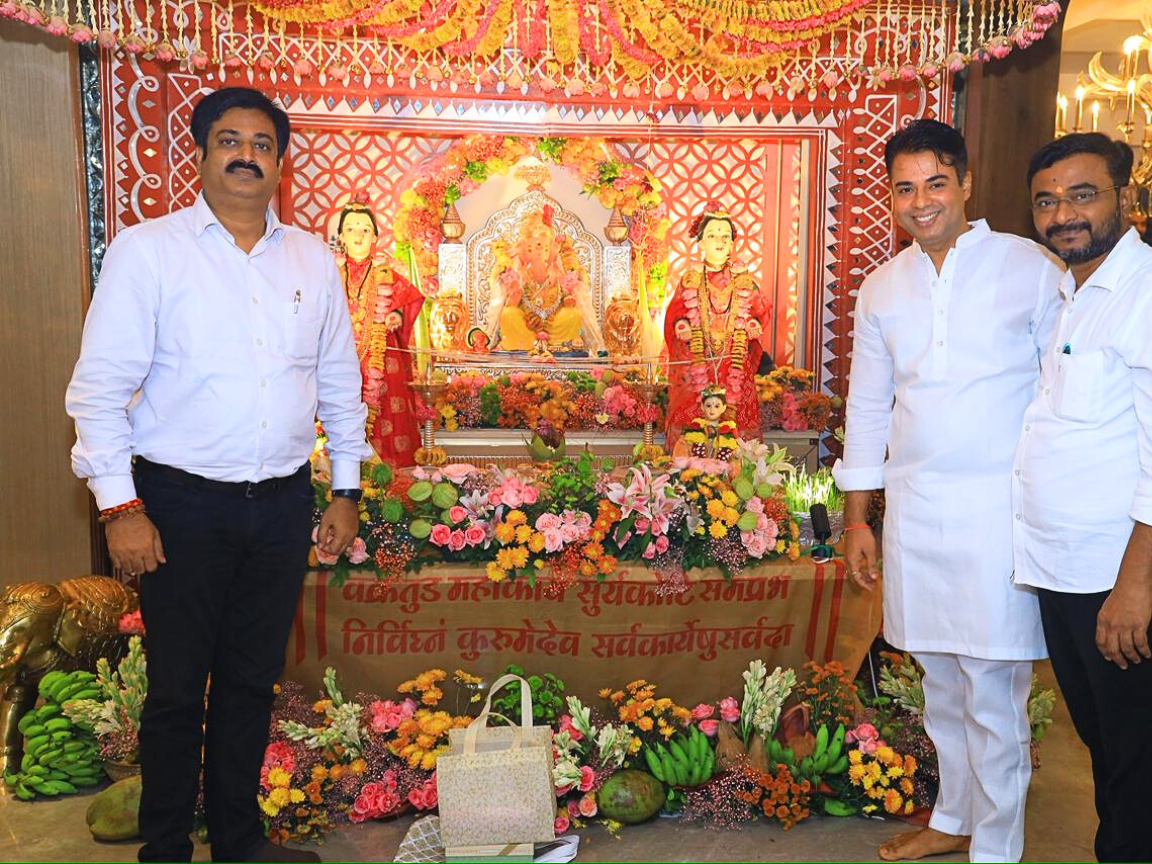 Sunil Keshary stands on the left side, Sankar Jha and another person stand to the right, with a beautiful large Ganpati decoration and floral arrangements in the background.